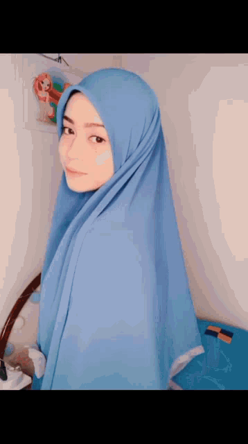 a woman wearing a blue hijab is standing in front of a wall with a picture of a girl on it