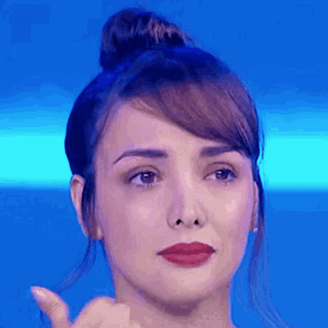 a close up of a woman 's face with a bun and red lipstick on a blue background .