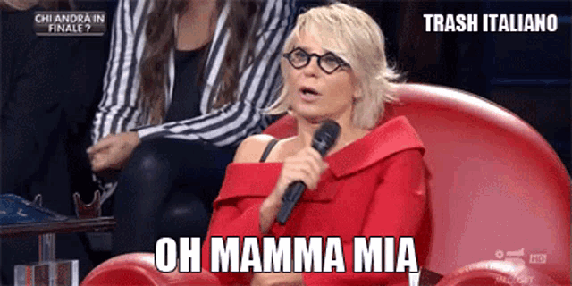 a woman sitting in a red chair holding a microphone and says oh mamma mia