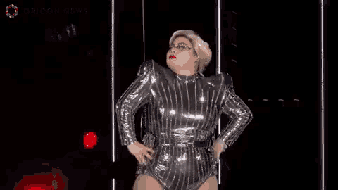 a woman in a silver bodysuit is dancing on a stage in front of a crowd .