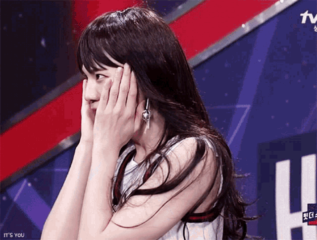 a woman covering her face with her hands in front of a tv screen that says " it 's you "