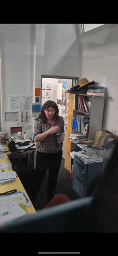 a woman in a leopard print shirt stands in a messy office