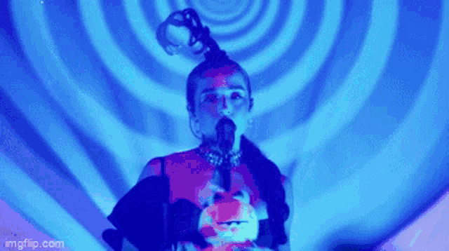 a woman is singing into a microphone while standing in front of a blue spiral .