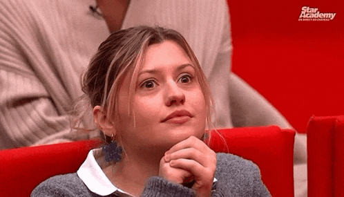 a woman is sitting in a red chair with her hands folded and looking at something .