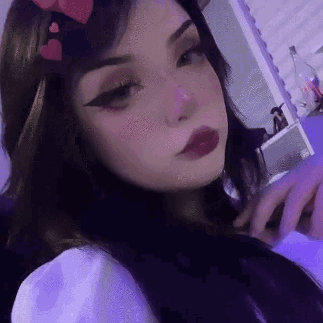 a girl with dark hair and red lipstick is taking a selfie with hearts on her head .