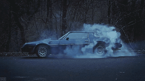 a blue car with smoke coming out of the tires is driving down a road