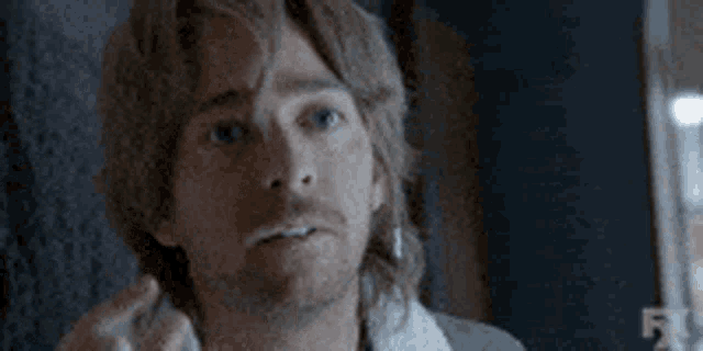 a man with a mullet and a beard is looking at the camera in a blurry photo .