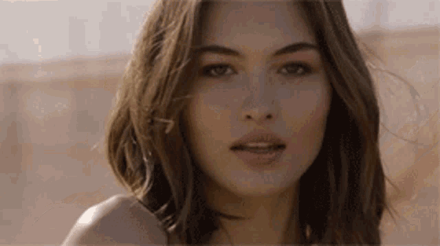 a close up of a woman 's face looking at the camera with her hair blowing in the wind .
