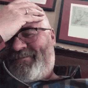 a man with a beard and glasses is holding his hand to his head .
