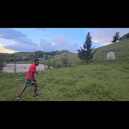 a man in a red shirt holds a bow and arrow in a field