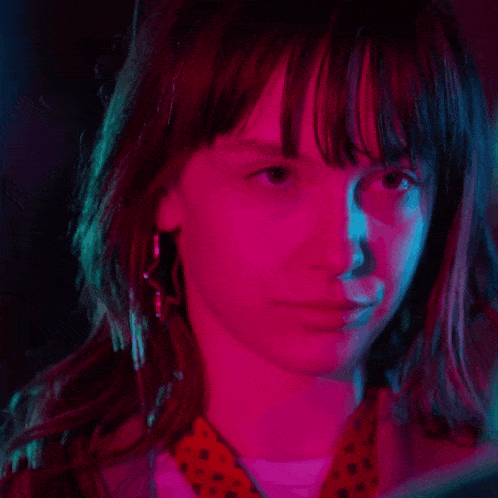 a close up of a woman 's face with a pink and blue light behind her