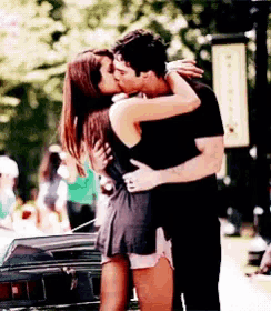 a man and a woman are kissing in front of a car on a street .