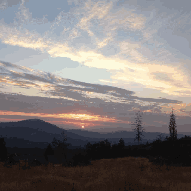 the sun is setting over the mountains and trees