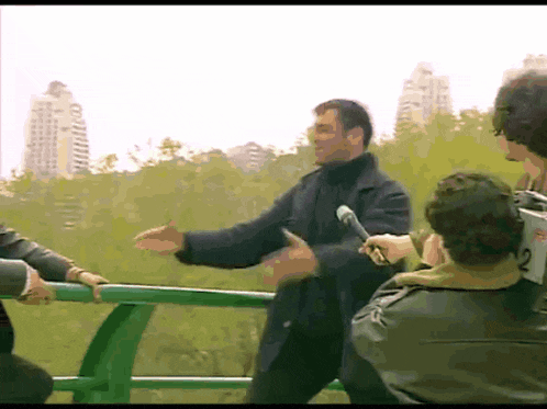a man in a black coat is being interviewed by a reporter with the number 2 on his back