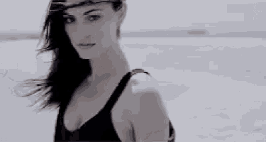 a woman in a black tank top is standing on a beach .