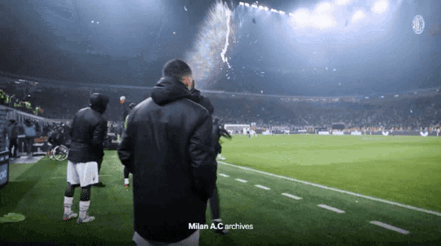 a man in a black jacket stands on a soccer field with milan a.c. archives written above him
