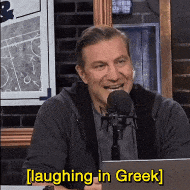 a man is laughing in front of a microphone with the words laughing in greek written below him