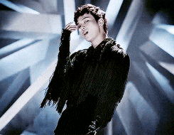 a man in a black fringed jacket stands in front of a blue background