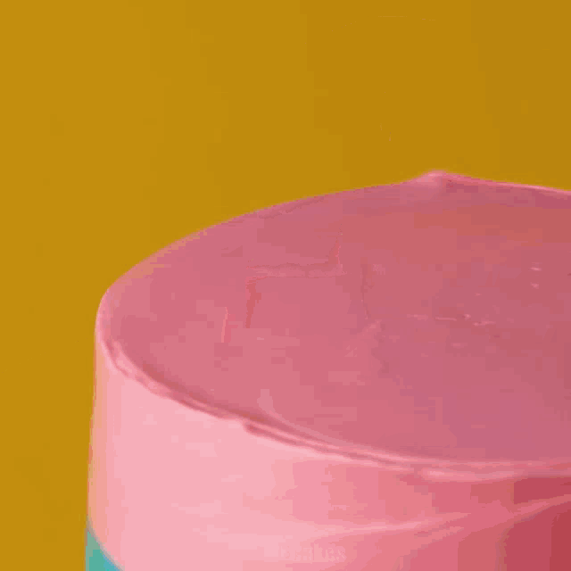 a cake with pink purple and teal frosting is on a wooden cutting board
