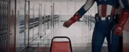 a man in a captain america costume is standing in a hallway next to a red chair .