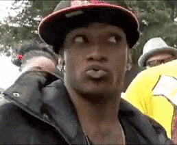 a man wearing a hat is making a funny face while standing in a crowd .