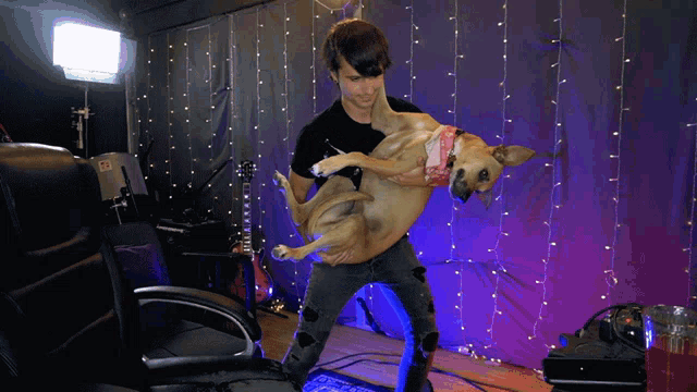 a man is holding a dog in his arms in front of a wall with lights