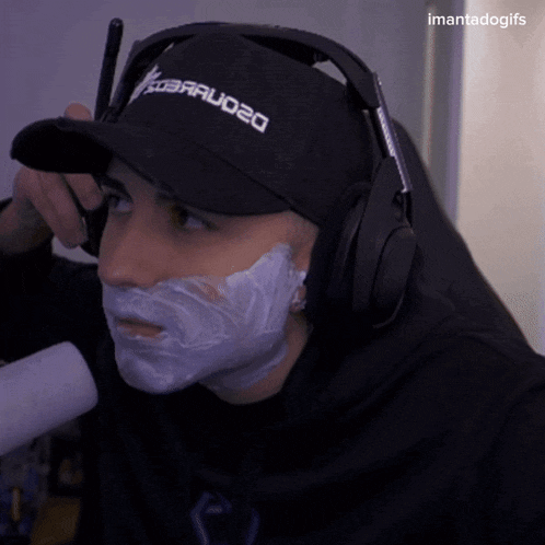 a man with shaving cream on his face is wearing headphones and a baseball cap that says barraudo20