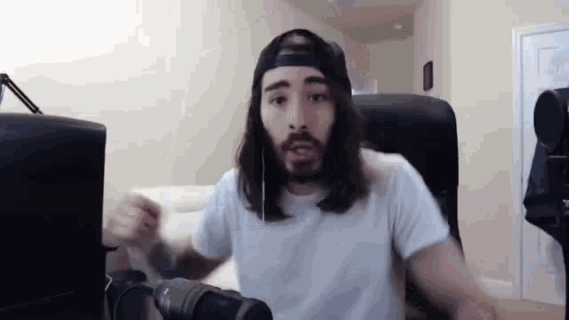 a man with long hair and a beard is sitting in front of a microphone in a living room .
