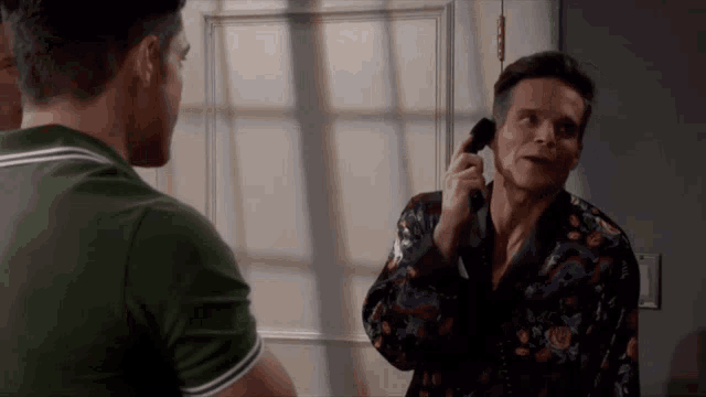 a man in a green shirt is talking on a cell phone while another man looks on .