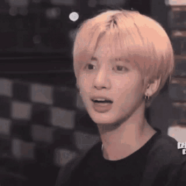 a close up of a young man with pink hair wearing a black shirt and earrings .