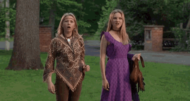 two women in purple dresses are dancing in a grassy field