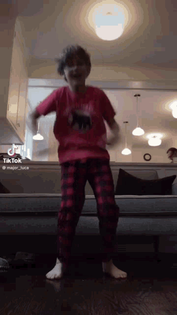 a boy in a red shirt and plaid pants is dancing in a living room .