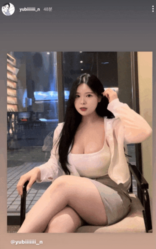 a woman in a white tank top sits in a chair with her legs crossed in front of a window ..