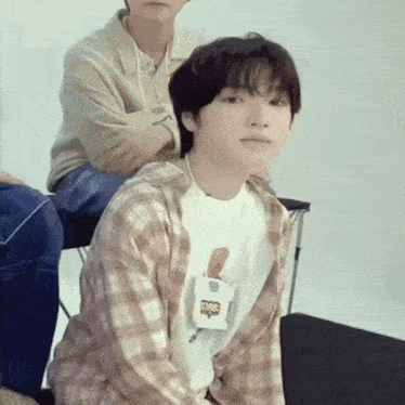 a young man wearing a plaid shirt and a white t-shirt with a bear on it looks at the camera