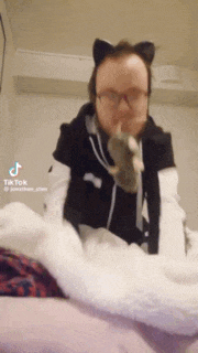 a man wearing cat ears and glasses is laying on a bed with a sock in his hand .