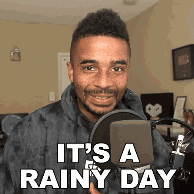 a man stands in front of a microphone with the words it 's a rainy day above him