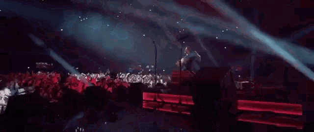 a man stands on a stage with a microphone in front of a crowd that is watching him