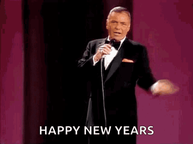 a man in a tuxedo is singing into a microphone with the words happy new years written below him .