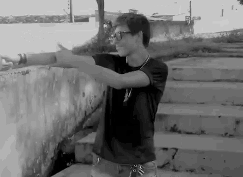 a young man wearing glasses and a black shirt is standing in front of a wall .