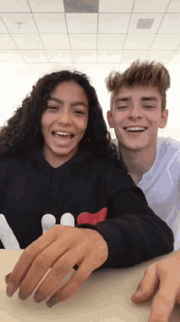 a boy and a girl are laughing together and the girl is wearing a black sweatshirt that says fila