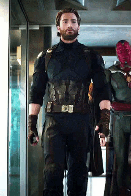 a man in a captain america uniform is standing next to a statue of vision .