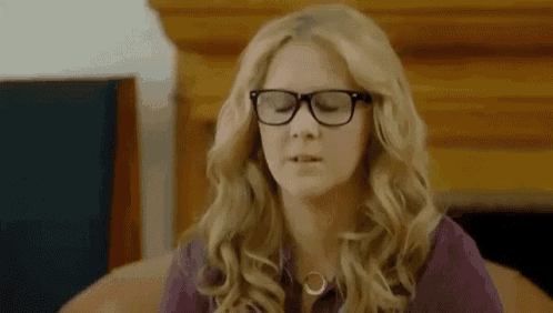 a woman wearing glasses and a necklace is sitting on a couch .