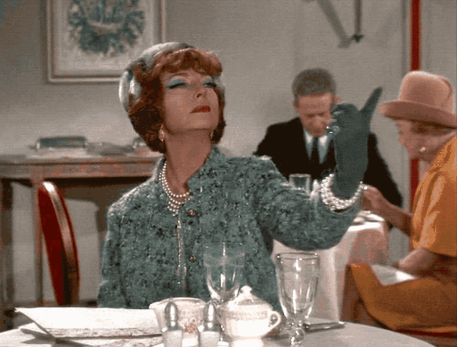 a woman sitting at a table wearing a pearl necklace and a blue jacket