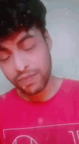 a man with a beard is wearing a red shirt and looking down .