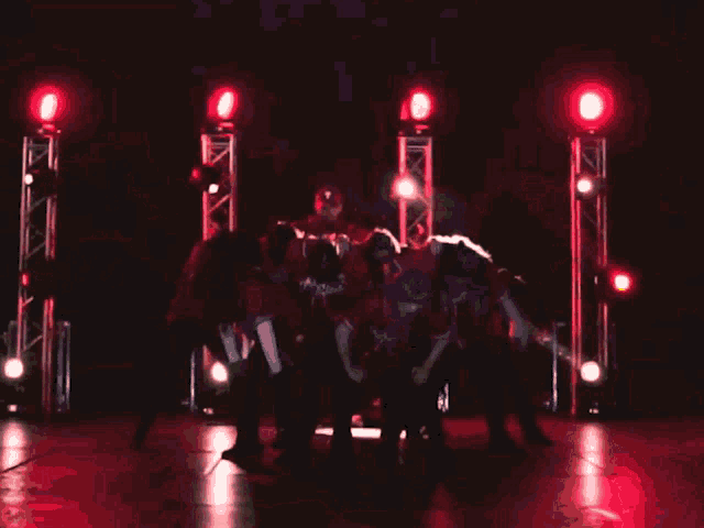 a group of people are dancing in front of a stage with red lights