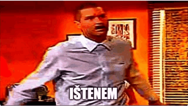 a man in a blue shirt is standing in front of a window with the word istenem written on his shirt .