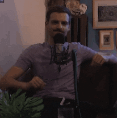 a man in a purple shirt is sitting in front of a microphone in a living room .