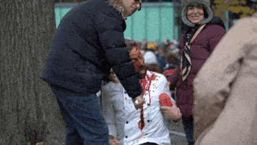 a man with blood on his face is being helped by a man in a jacket