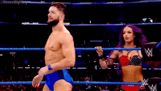 a man in a blue trunks is standing in a wrestling ring with a woman in a bikini .