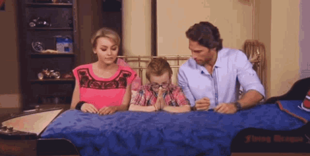a woman in a pink top sits next to a man and a boy on a blue blanket